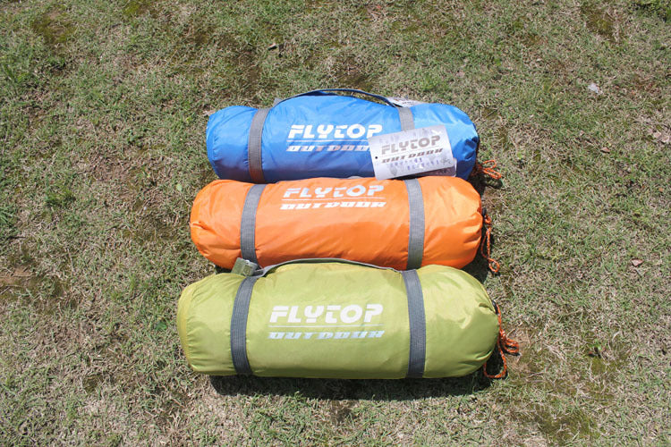 Three rolled-up Outdoor Double Camping Rainproof Tents in blue, orange, and green rest on the grass. Each ultra-light tent, perfect for high-altitude mountaineering in snowfields, features the brand name eprolo emblazoned in white lettering.