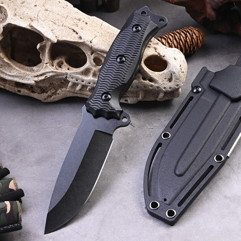 The A3 High Hardness Outdoor Multifunctional Portable Knife by eprolo, perfect for survival, features a textured handle and sits on a gray surface with its sheath. An animal skull and rope coil provide the backdrop, while camouflage fabric is visible from the left.