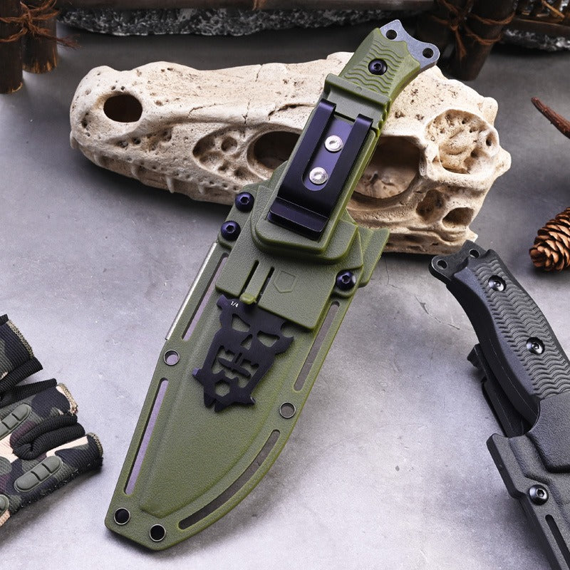 The eprolo A3 High Hardness Outdoor Multifunctional Portable Knife, featuring a green textured handle and black sheath with rivets and clip, rests on a gray surface. It is ideal for outdoor adventures with pinecones, gloves, and a rugged rock nearby.