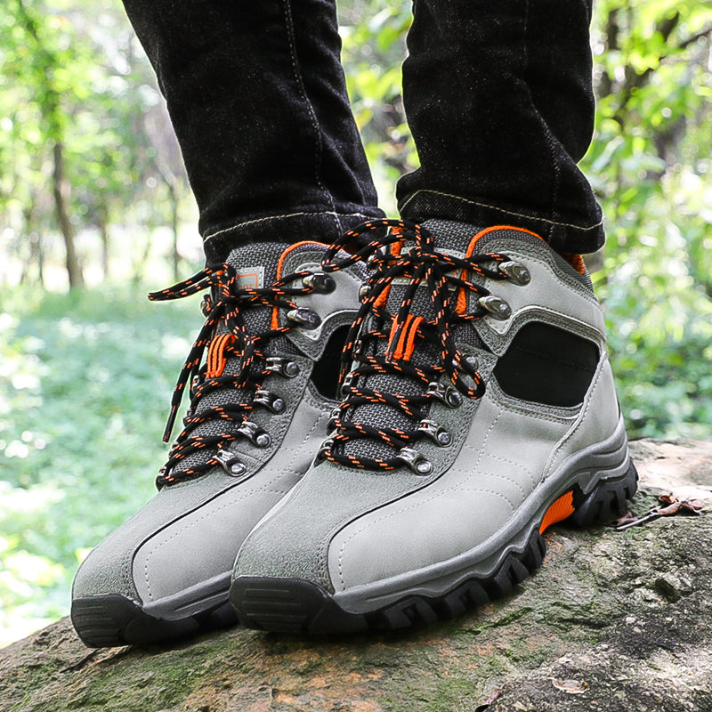 In a forested area, someone stands on a rock wearing My Store’s Breathable Waterproof Hiking Sneakers with anti-slip soles and orange-black laces. Black pants peek out amid lush greenery, promising an adventurous journey with every step.