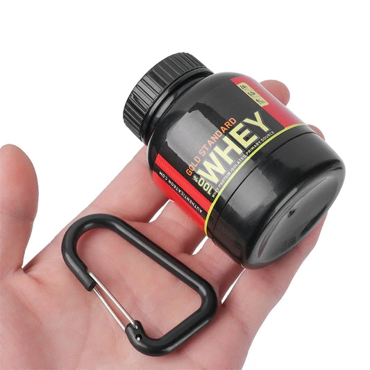 A hand holds a small black container labeled GOLD STANDARD WHEY with red and gold accents. Next to it is the Ten Essentials Mini Portable Protein Powder Bottle – Travel Funnel & Storage with Keychain, ideal for on-the-go use.