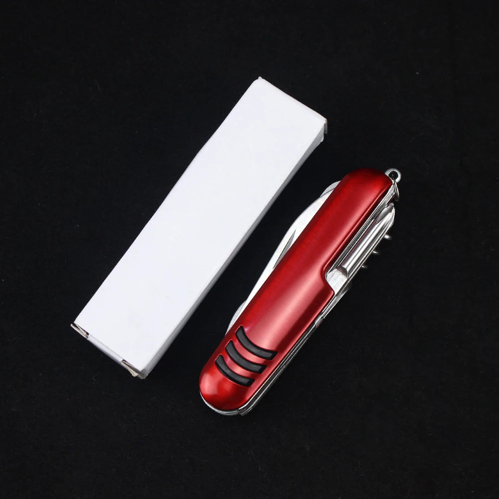 The Ten Essentials 11-in-1 Swiss Folding Pocket Knife, a multifunctional keychain multitool crafted from durable stainless steel, rests beside a closed white box on a black surface.