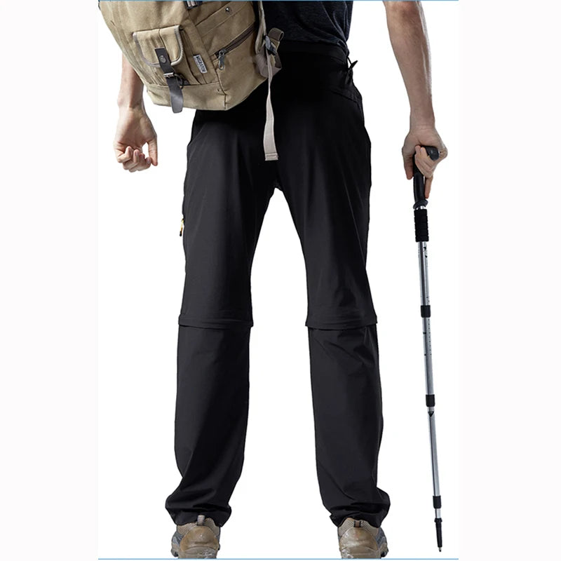 A person wearing Ten Essentials Mens Convertible Quick-Dry Stretch Cargo Hiking Pants, with trekking pole and beige backpack, shows off the full length of their black pants paired with tan hiking shoes—perfectly geared for outdoor adventure.