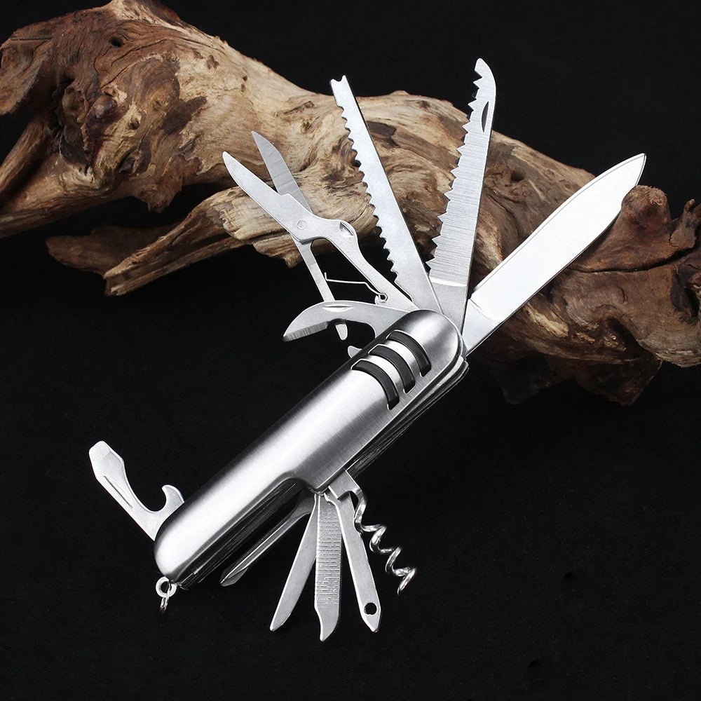 This Ten Essentials 11-in-1 Swiss Folding Pocket Knife is a stainless steel multitool featuring a blade, scissors, saw, corkscrew, and bottle opener. It’s showcased extended against a black background and driftwood.