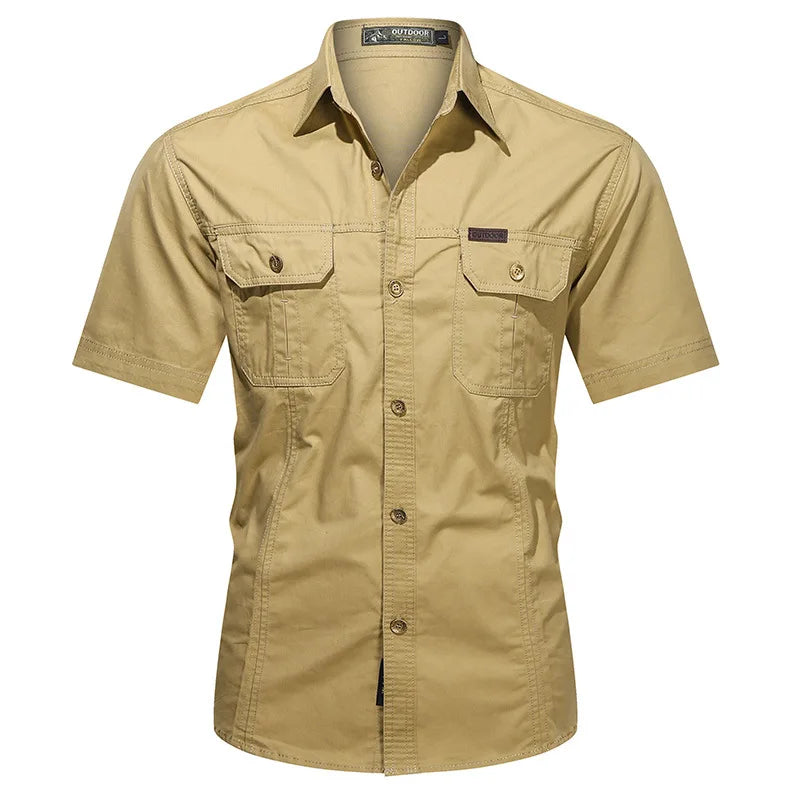 The Men’s Quick-Dry Tactical Shirt by Ten Essentials is a beige, short-sleeve, breathable cotton shirt with a collar and two front pockets, featuring a left pocket patch and military-inspired design ideal for outdoor activities.