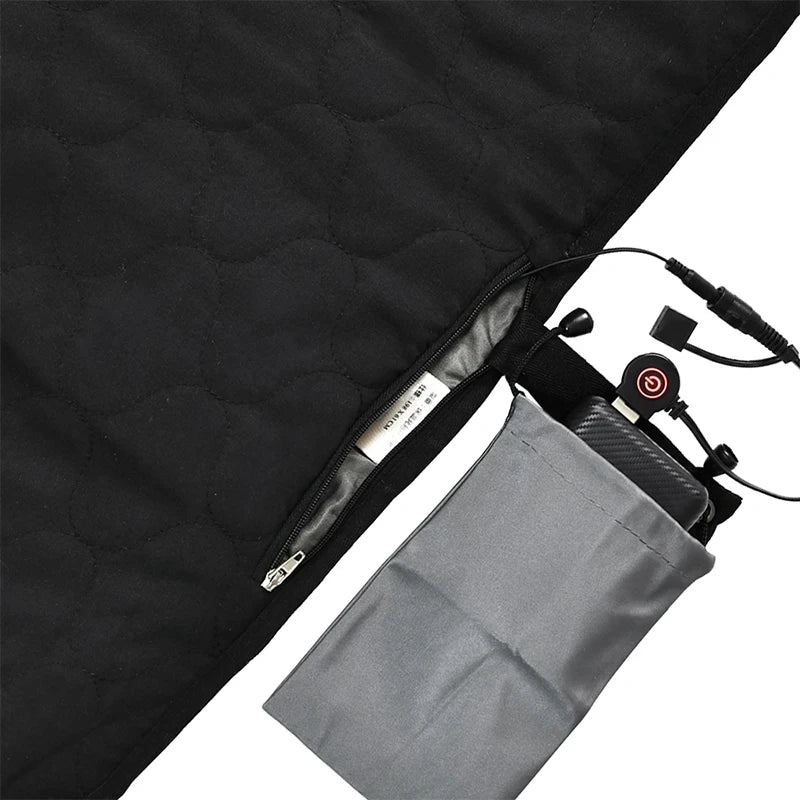 Close-up of the black quilted USB Heated Sleeping Bag Pad by Ten Essentials shows a partially open zipper with an inner label. A gray pocket holds a control device connected by wires, featuring black buttons for adjustable 3-level temperature on this fast-heating camping mat.