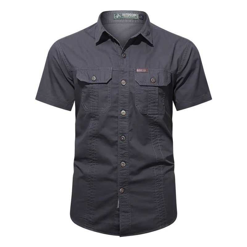 The Ten Essentials Mens Quick-Dry Tactical Shirt in dark gray is a short-sleeve button-up made from breathable cotton. It has a military-inspired design, double chest pockets, brown buttons, subtle stitching, a collar, and an embroidered logo above the left pocket.