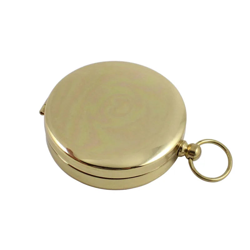 The Ten Essentials Portable Water-Resistant Luminous Brass Compass is a round, closed tool perfect for outdoor adventures. It features a small side ring for easy carrying and its smooth, shiny surface subtly reflects light, making it an essential aid in survival situations.