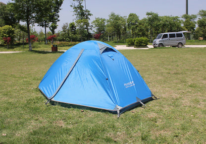 An eprolo Outdoor Double Camping Rainproof Tent is pitched on a grassy field beneath a clear sky, encircled by trees, with a gray van in the background.