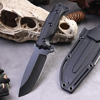 The A3 High Hardness Outdoor Multifunctional Portable Knife by eprolo, perfect for survival, features a textured handle and sits on a gray surface with its sheath. An animal skull and rope coil provide the backdrop, while camouflage fabric is visible from the left.