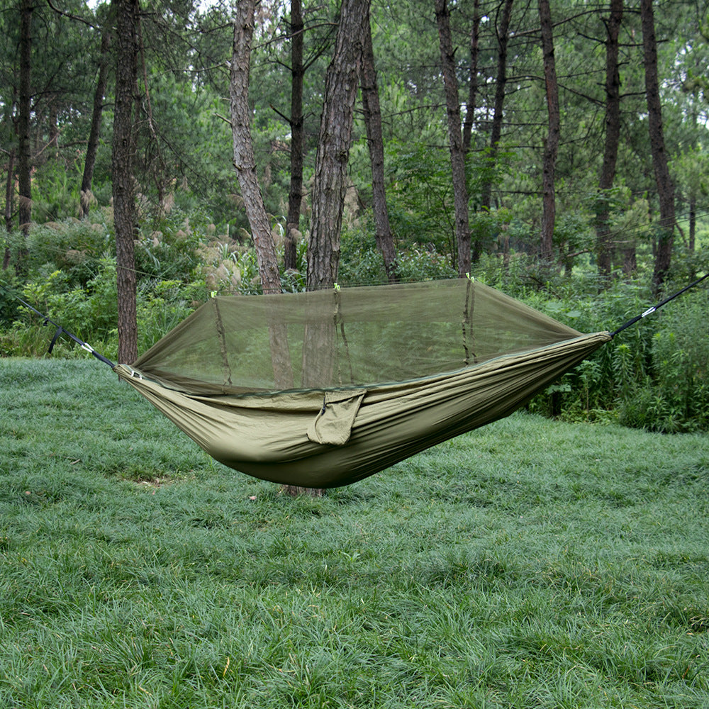 The eprolo Portable Camping Hammock with Mosquito Net, made from 210T Parachute Nylon, hangs between trees in a lush forest. The ground is blanketed with green grass, and tall trees tower in the background, creating a serene and relaxing setting.