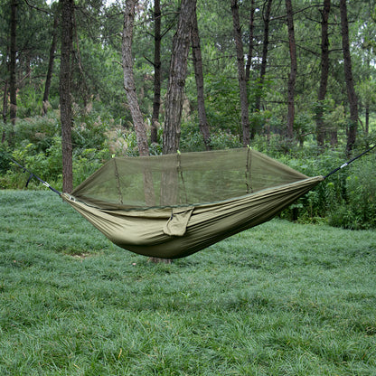 The eprolo Portable Camping Hammock with Mosquito Net, made from 210T Parachute Nylon, hangs between trees in a lush forest. The ground is blanketed with green grass, and tall trees tower in the background, creating a serene and relaxing setting.