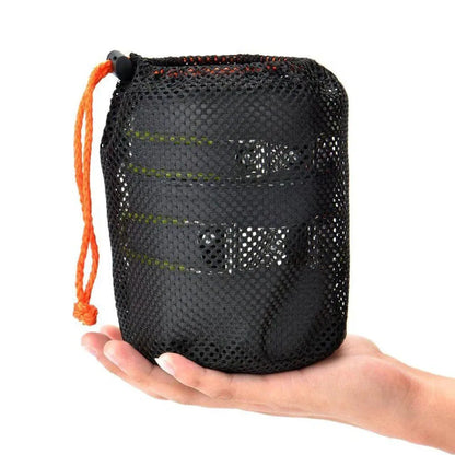 A hand grips a black mesh bag with an orange drawstring, revealing the Ten Essentials Camping Cookware Kit with Stove. This lightweight set features stacked pots, ideal for hiking and travel adventures.