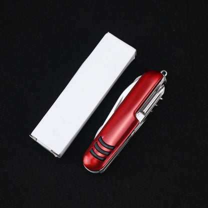 The Ten Essentials 11-in-1 Swiss Folding Pocket Knife, a multifunctional keychain multitool crafted from durable stainless steel, rests beside a closed white box on a black surface.