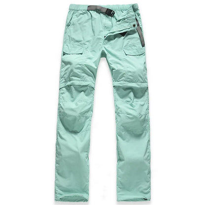 The NUONEKO Women’s Convertible Hiking Pants by Ten Essentials are light green, with multiple pockets, a dark belt, quick-dry fabric, knee stitching, and a zipper fly. Ideal for adventures, they are laid flat on a white background to showcase their features.