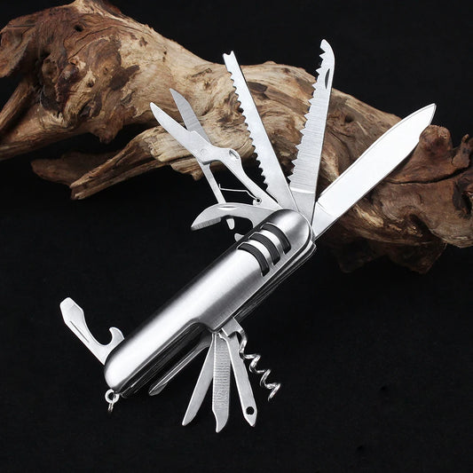 This Ten Essentials 11-in-1 Swiss Folding Pocket Knife is a stainless steel multitool featuring a blade, scissors, saw, corkscrew, and bottle opener. It’s showcased extended against a black background and driftwood.