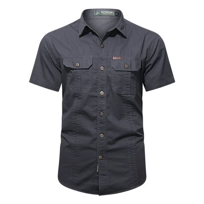 The Ten Essentials Mens Quick-Dry Tactical Shirt in dark gray is a short-sleeve button-up made from breathable cotton. It has a military-inspired design, double chest pockets, brown buttons, subtle stitching, a collar, and an embroidered logo above the left pocket.