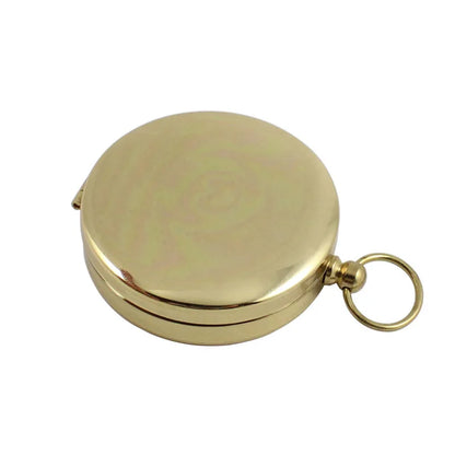 The Ten Essentials Portable Water-Resistant Luminous Brass Compass is a round, closed tool perfect for outdoor adventures. It features a small side ring for easy carrying and its smooth, shiny surface subtly reflects light, making it an essential aid in survival situations.