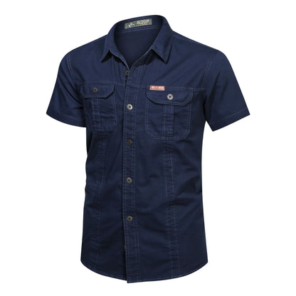 The Men’s Quick-Dry Tactical Shirt by Ten Essentials is navy blue, short-sleeve, and made of breathable cotton. It features two front button-flap pockets, visible stitching, a subtle label on the left pocket, and offers a rugged yet stylish military-inspired design.
