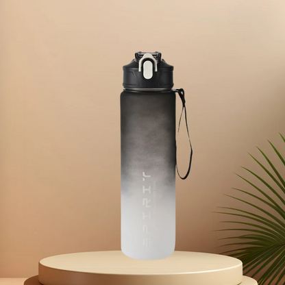 A stylish Ten Essentials sports water bottle with a black-and-white gradient stands on a round pedestal. It boasts a leak-proof flip-top lid, carrying strap, and the word SPIRIT printed vertically. A small green plant partially peeks in on the right against beige surroundings.